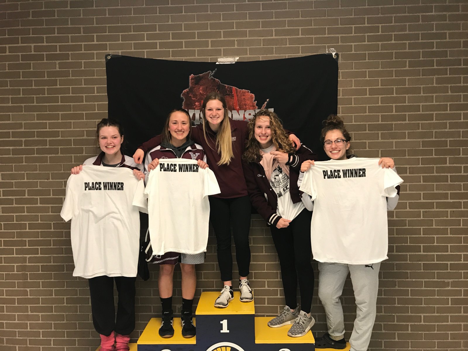 Holmen wrestlers holding Place Winner shirts on a podium, 2017-2018 season
