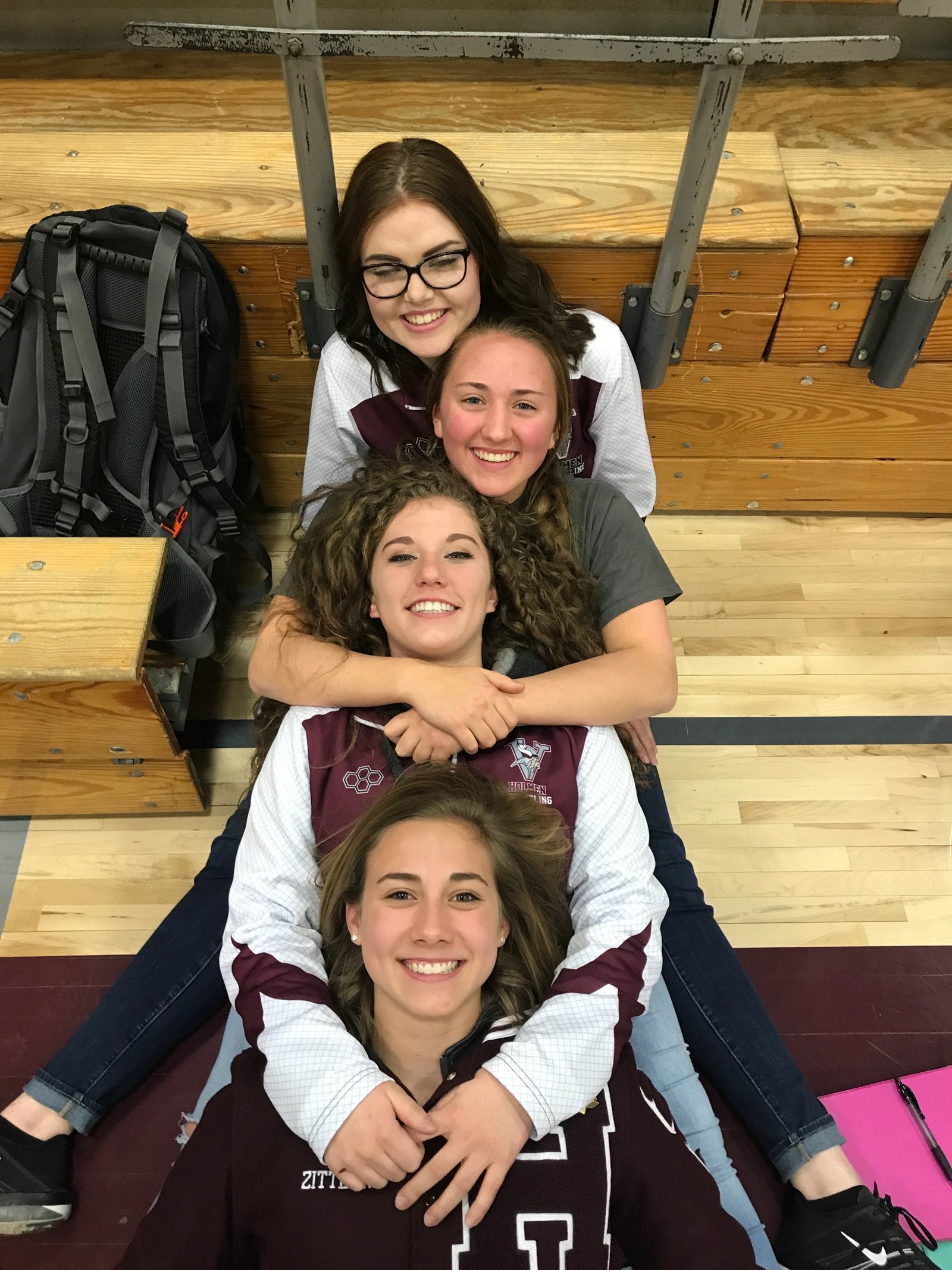 Four Holmen wrestlers piled together and smiling in the bleachers, 2017-2018 season